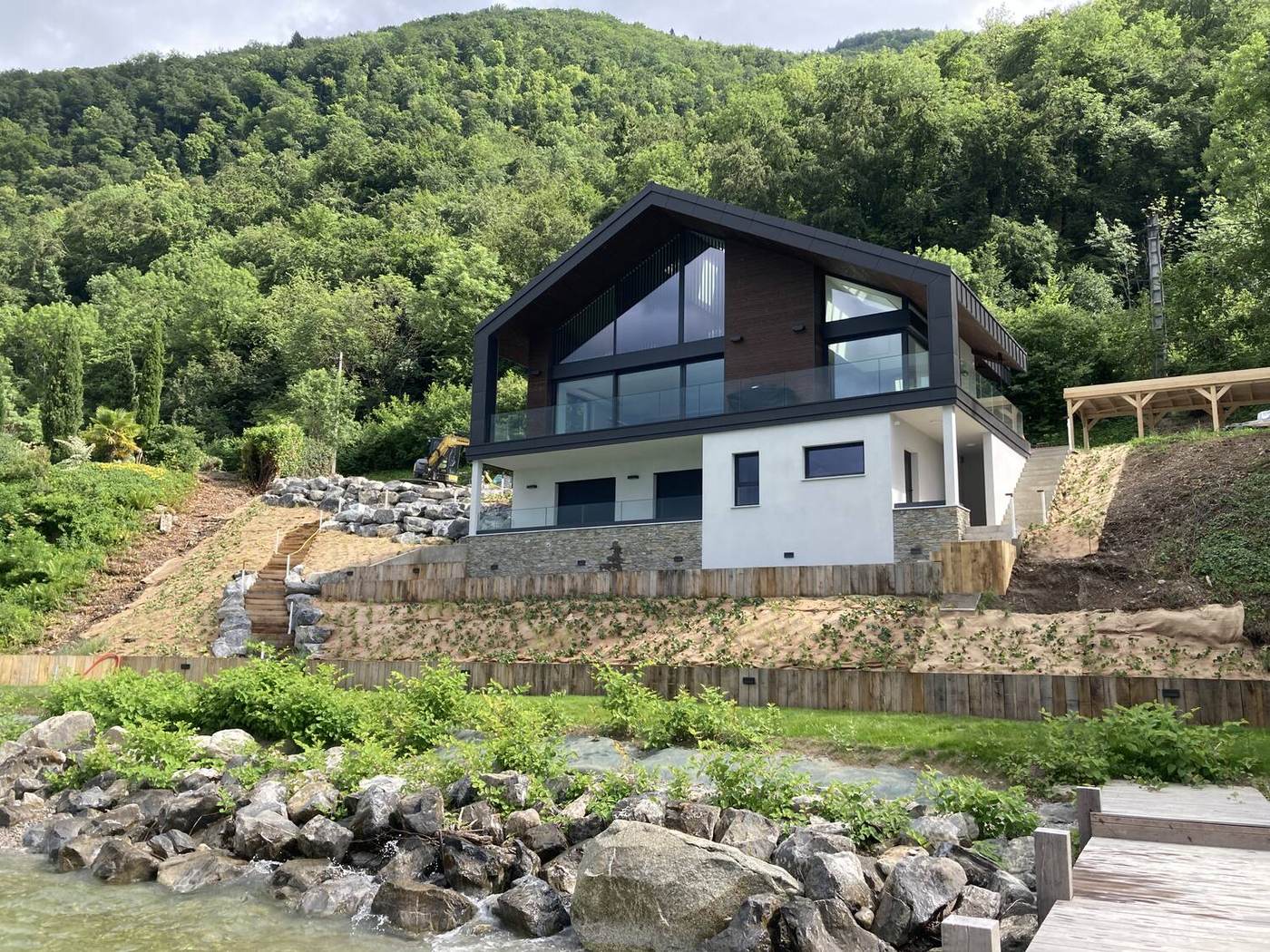 La maison vue depuis la rive, toiture asymétrique et grandes baies sombres